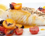 Pyszny halibut ryba, pieczony z pomidorkami koktajlowymi i ziołami, podany z cytryną.