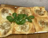 Sześć kwadratowych porcji ciasta francuskiego z mięsem mielonym i serem, ozdobione listkami bazylii.