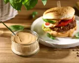 Pyszny sos do burgera w słoiczku, obok apetyczny burger z dodatkami. Idealny duet na letni wieczór.