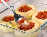 Łyżka nakłada mięsne nadzienie do wgłębień w ziemniaczanych grule, przygotowywanych w szklanym naczyniu.