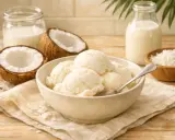 Pyszne, kremowe domowe lody kokosowe w misce, obok połówki kokosa, mleka i wiórków.