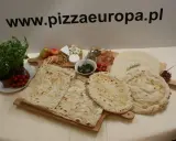 Gotowe ciasto na pizzę, świeże zioła, pomidorki, ser i inne dodatki na drewnianych deskach. Idealne na domowe wypieki.