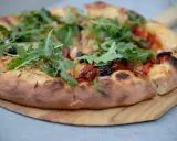 Idealne ciasto na pizzę z rukolą, oliwkami i papryką, wypieczone na drewnianej desce.
