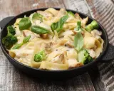 Tradycyjna potrawka z kurczaka z makaronem tagliatelle, brokułami i kremowym sosem, udekorowana świeżą bazylią.