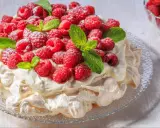 Beza Pavlova, która zawsze wychodzi, udekorowana świeżymi malinami i listkami mięty, posypana cukrem pudrem.