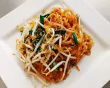 Pyszne pad thai co to? Danie z makaronem ryżowym, kiełkami fasoli mung, jajkiem i szczypiorkiem na białym talerzu.