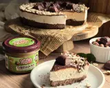 Pyszne ciasto kinder bueno z mascarpone, udekorowane orzechami i kawałkami czekolady. Obok słoik pasty z orzechów laskowych.