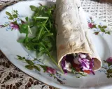 Pyszny lawasz kebab z czerwoną kapustą, pomidorem i rukolą na ozdobnym talerzu.