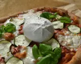 Pyszna pizza z burrata, cukinią i bazylią, posypana świeżo mielonym pieprzem.