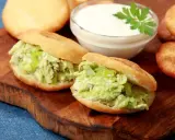 Dwie pyszne arepas z kurczakiem i awokado, obok miseczka sosu i kilka niefaszerowanych arepas.