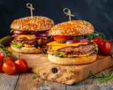 Dwa soczyste burgery z idealnie wysmażonym mięsem na burgery, serem, warzywami i sezamową bułką, podane na drewnianej desce z pomidorkami.