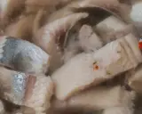 Kawałki kiszonych śledzi w zalewie, z widocznymi fragmentami skórki i przyprawami.