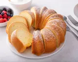 Puszysta, pokrojona wielkanocna babka posypana cukrem pudrem, obok miseczka z jagodami i malinami.
