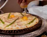 Kucharz dodaje jajko do pizzy z boczkiem i szparagami. Pyszna pizza z jajkiem w przygotowaniu.