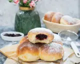 Najprostsze drożdżówki z dżemem, posypane cukrem pudrem, kuszą swoim wyglądem. W tle widać koszyk z kolejnymi wypiekami i wazon z kwiatami.