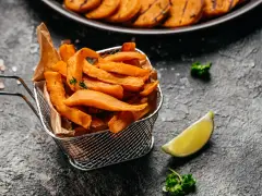Chrupiące frytki z batatów z frytkownicy airfryer, podane w metalowym koszyku, z limonką i natką pietruszki.