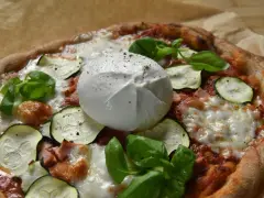 Pyszna pizza z burrata, cukinią i bazylią, posypana świeżo mielonym pieprzem.