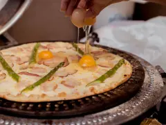 Kucharz dodaje jajko do pizzy z boczkiem i szparagami. Pyszna pizza z jajkiem w przygotowaniu.