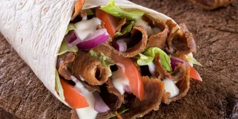 Pyszny, domowy kebab zawinięty w tortillę z soczystym mięsem, chrupiącą sałatą, pomidorami i cebulą, polany sosem.