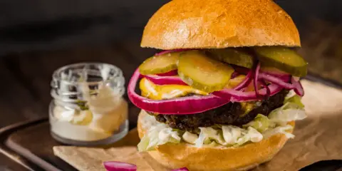 Soczysty burger z ogórkiem, czerwoną cebulą i majonezem, idealny do przygotowania, jak smażyć burgera na patelni.