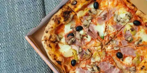 Pizza capricciosa z szynką, pieczarkami, karczochami i czarnymi oliwkami, w pudełku.