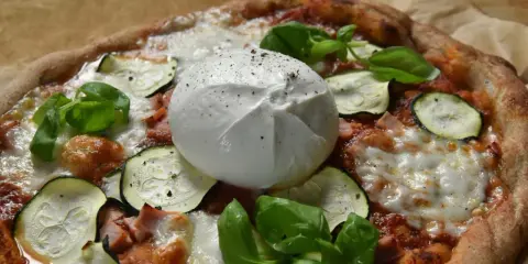 Pyszna pizza z burrata, cukinią i bazylią, posypana świeżo mielonym pieprzem.