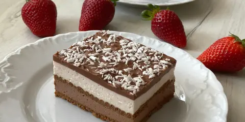 Mega szybkie ciasto bez pieczenia z warstwami czekolady i śmietanki, posypane wiórkami kokosowymi. Obok świeże truskawki.