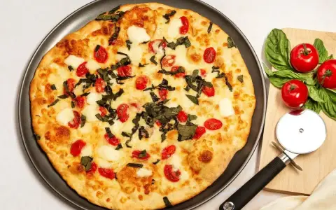 Pyszna pizza z serka wiejskiego, pomidorkami koktajlowymi i bazylią. Obok leży nóż do pizzy i świeże pomidory.