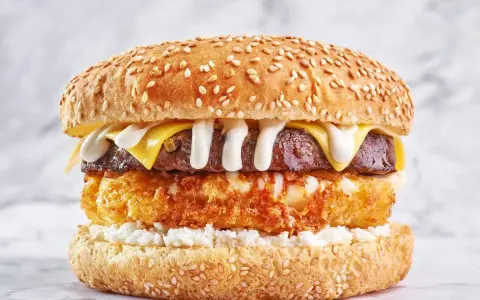 Apetyczny burger drwala przepis: soczysta wołowina, chrupiące panierowane ziemniaki, ser i biały sos na sezamowej bułce.