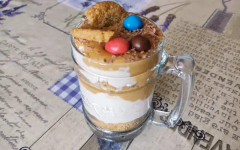 Warstwowy deser banoffee w szklance z polewą karmelową, bitą śmietaną, ciasteczkami i kolorowymi drażetkami.