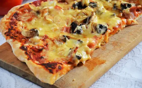 Pyszna pizza capriciosa z pieczarkami i szynką, roztopiony ser ciągnie się na chrupiącym cieście.