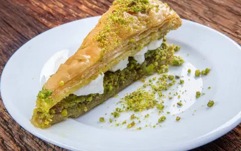 Pyszna baklawa z pistacjami i kremem na białym talerzu. Idealny przepis na deser.
