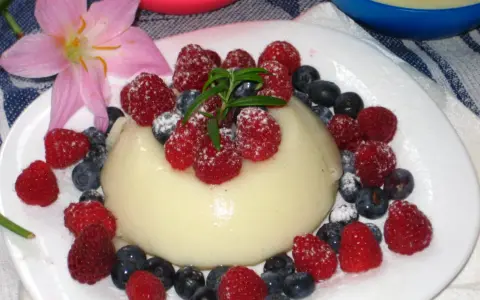 Panna cotta z malinami i borówkami, posypana cukrem pudrem. Idealny deser, który można zrobić według prostego legumina przepisu.