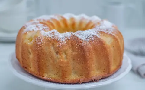 Szybka babka wilgotna, oprószona cukrem pudrem, prezentuje się apetycznie na białej paterze. Idealna na szybką przekąskę.
