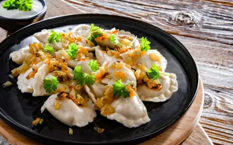Pyszne pierogi ukraińskie, polane skwarkami i posypane natką pietruszki, podane z miseczką śmietany.