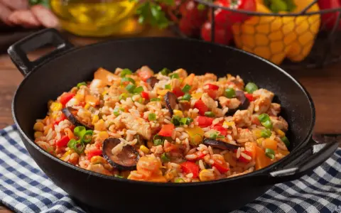Pyszne jambalaya z kurczakiem, kiełbasą, kukurydzą i papryką w czarnej patelni.