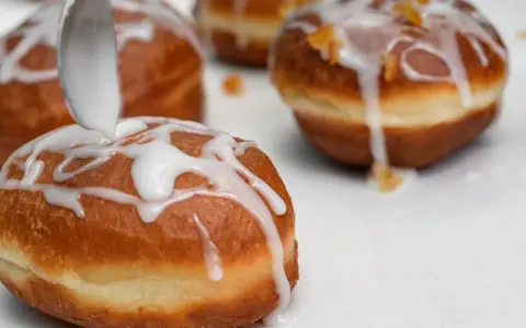 Lukier przepis na pączki. Łyżka polewa słodką masą pączki, które zaraz trafią na stół.