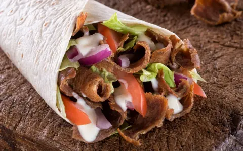 Pyszny, domowy kebab zawinięty w tortillę z soczystym mięsem, chrupiącą sałatą, pomidorami i cebulą, polany sosem.
