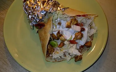 Pyszny kebab w tortilli z kurczakiem, warzywami i sosem na zielonym talerzu.