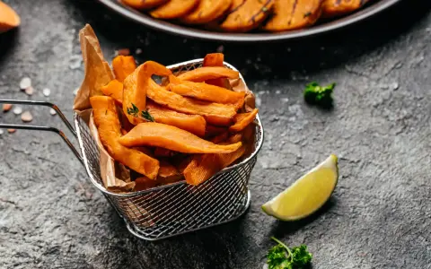 Chrupiące frytki z batatów z frytkownicy airfryer, podane w metalowym koszyku, z limonką i natką pietruszki.