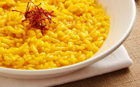 Aksamitne risotto alla milanese, złociste od szafranu, podane w białej misce, ozdobione nitkami szafranu.