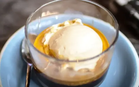 Pyszne affogato: gałka lodów waniliowych w gorącym espresso, podana w szklance na niebieskim talerzyku.