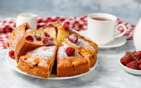Błyskawiczne i super łatwe ciasto z owocami, posypane cukrem pudrem, z malinami i filiżanką herbaty.