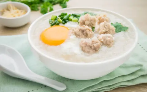 Miseczka aromatycznego congee z mięsnymi klopsikami, jajkiem i szczypiorkiem.