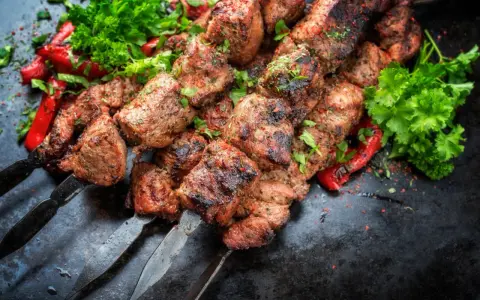 Soczyste kawałki mięsa na szpadach, przypominające kofta kebab, podane z pieczoną papryką i świeżą natką pietruszki.