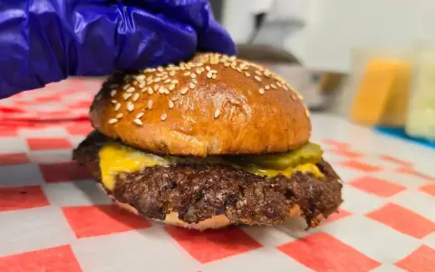 Rękawiczka w niebieskiej rękawiczce przygotowuje pysznego smash burgera z serem i ogórkiem.