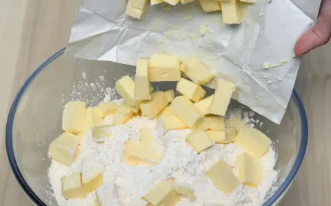 Kawałki zimnego masła dodawane do mąki w misce, kluczowy krok w sprawdzonym przepisie na kruche ciasto.