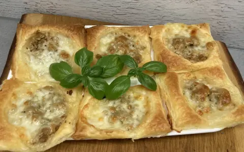Sześć kwadratowych porcji ciasta francuskiego z mięsem mielonym i serem, ozdobione listkami bazylii.