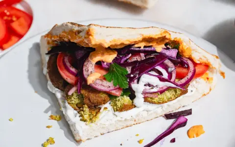 Pyszny falafel kebab w bułce z pomidorami, czerwoną cebulą, kapustą i sosami.