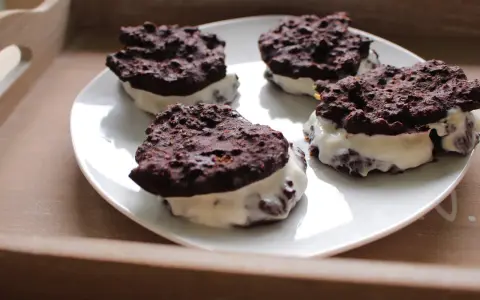 Cztery domowe ciastka Oreo z kremowym nadzieniem, ułożone na białym talerzu.